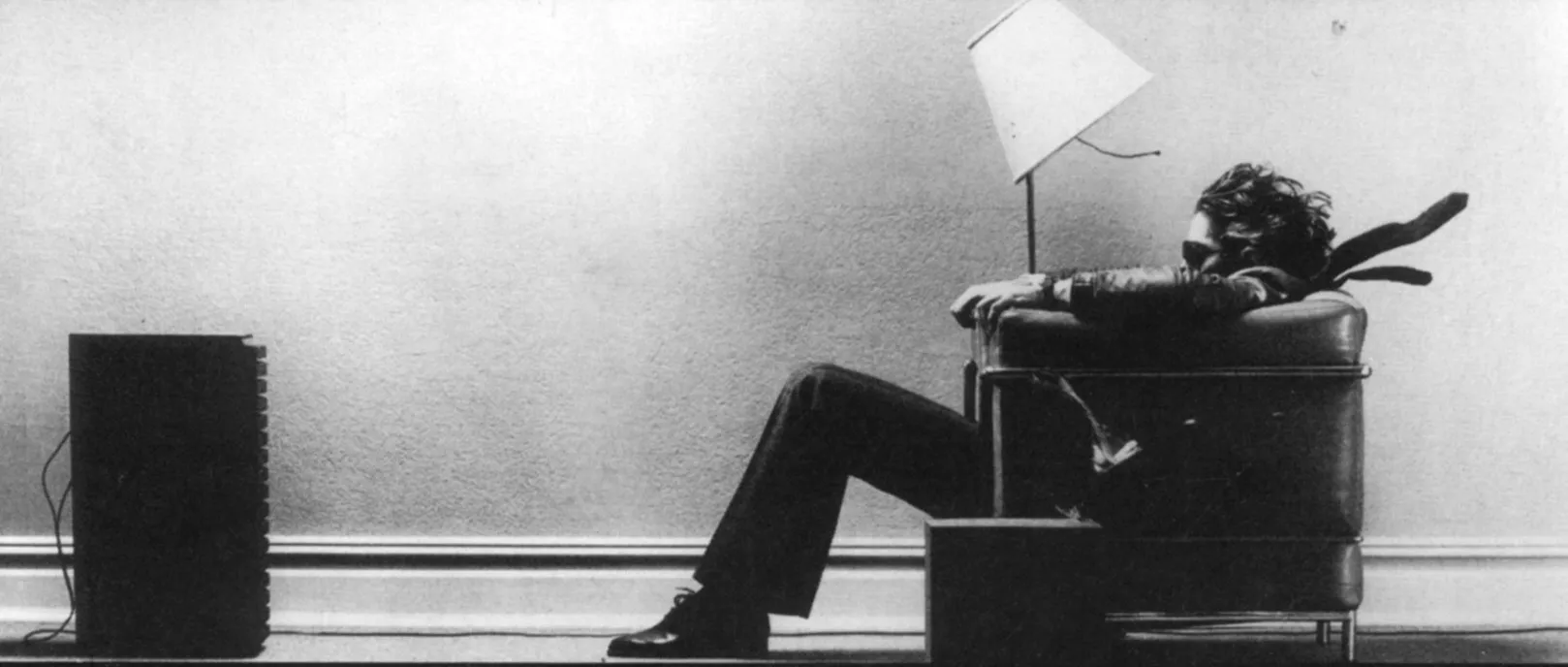 A man sits in a low
chair in front of speakers that sit on his floor. His hair, necktie, and the
lampshade are being blown backward.